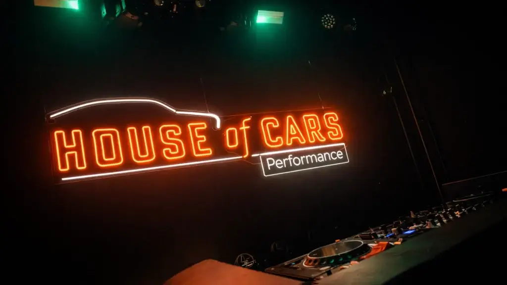 Maatwerk neonbord met tekst HOUSE of CARS Performance, geproduceerd door Living Lumen en gemonteerd op een zwarte muur in een eventlocatie.
