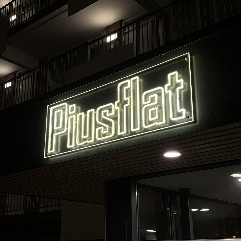 LED neon gevelreclame Piustflat op appartementencomplex in de avond